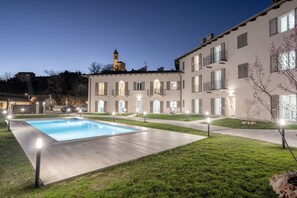 A modern building with a swimming pool, outdoor lighting, and a tower in the background. - Katia House - Apartment the Lilies (Castelnuovo Calcea)