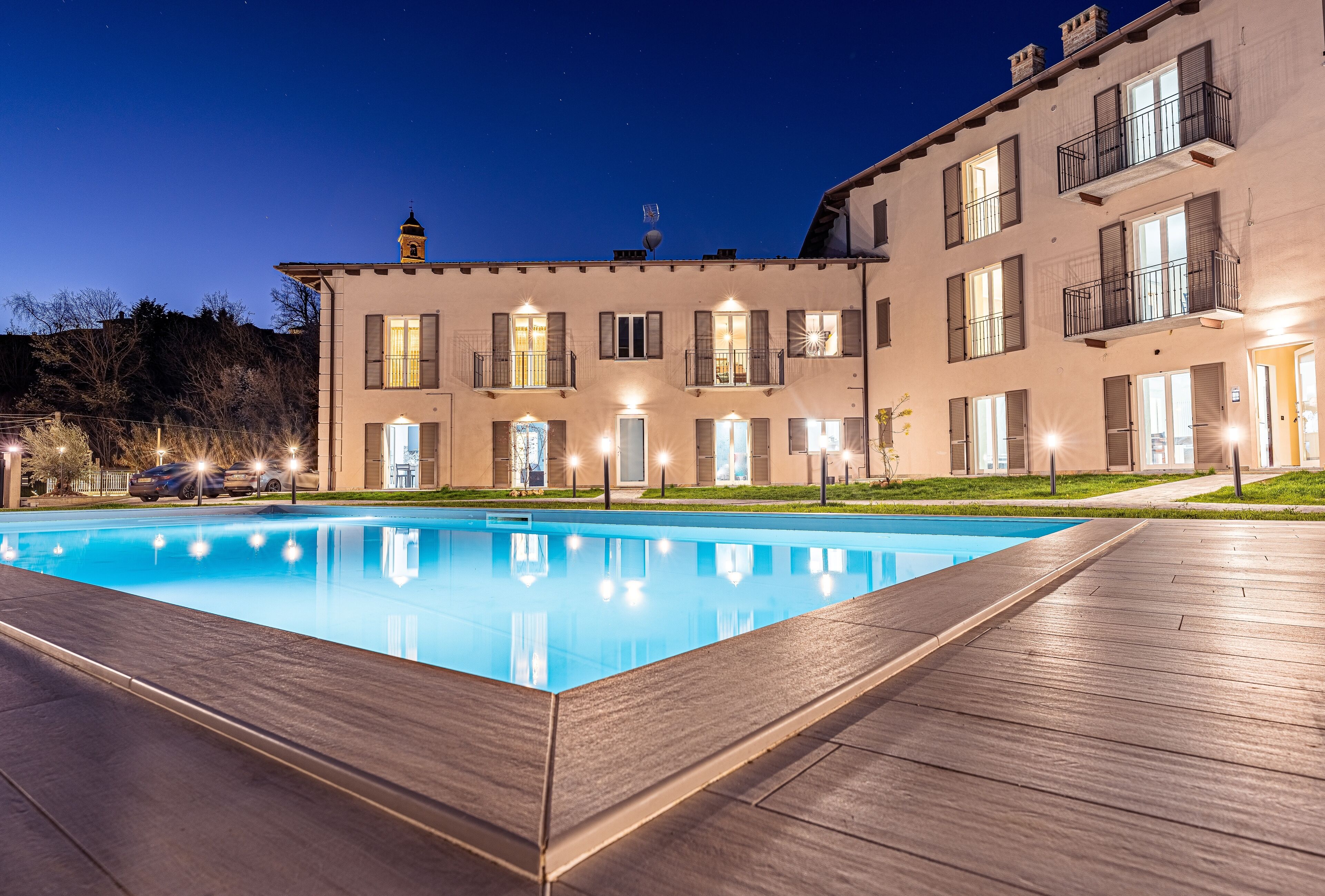 Une piscine avec une terrasse en bois, un bâtiment doté de nombreuses fenêtres et de balcons, et un ciel nocturne dégagé.