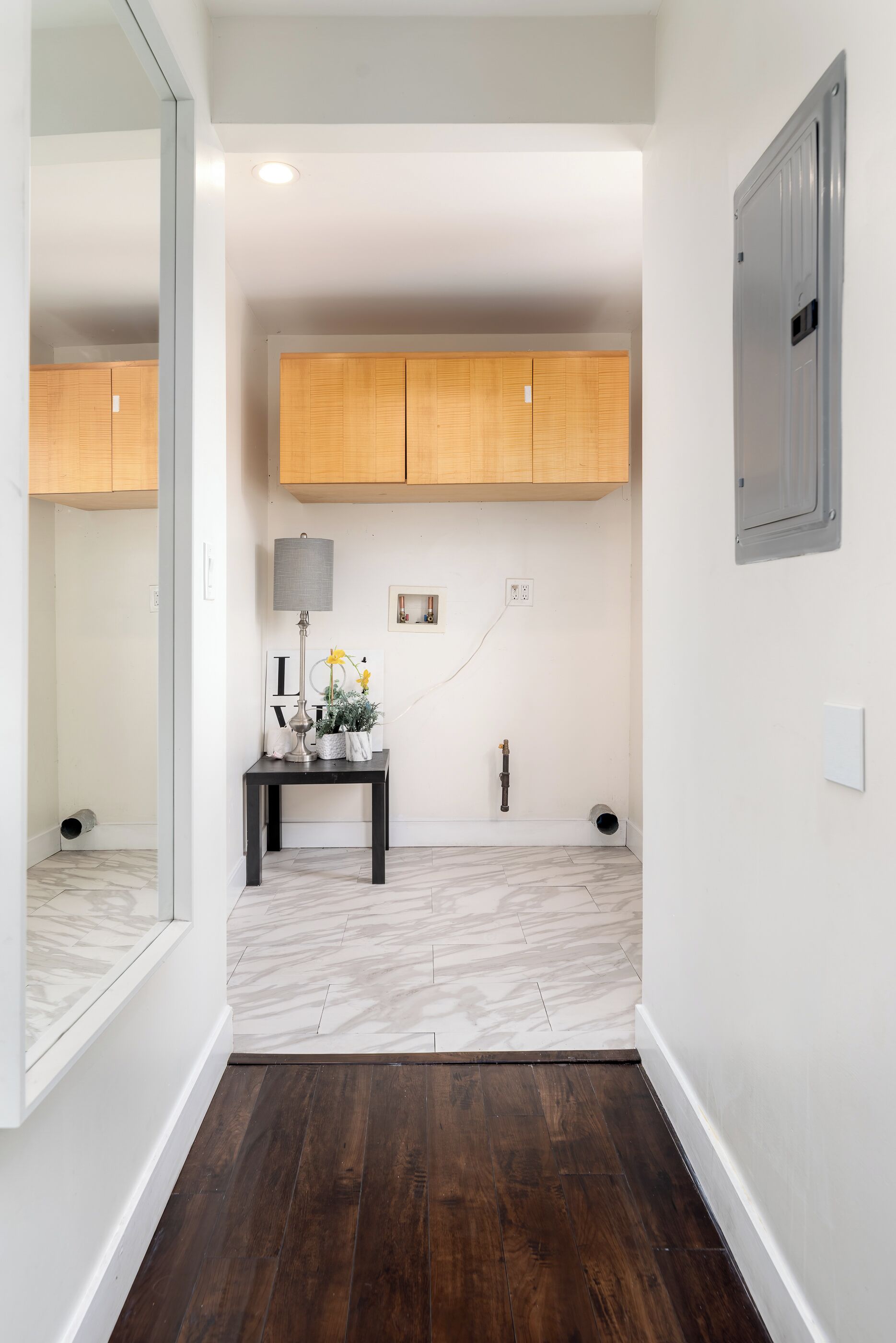 Un couloir avec un meuble en bois, une petite table avec une lampe et un miroir.