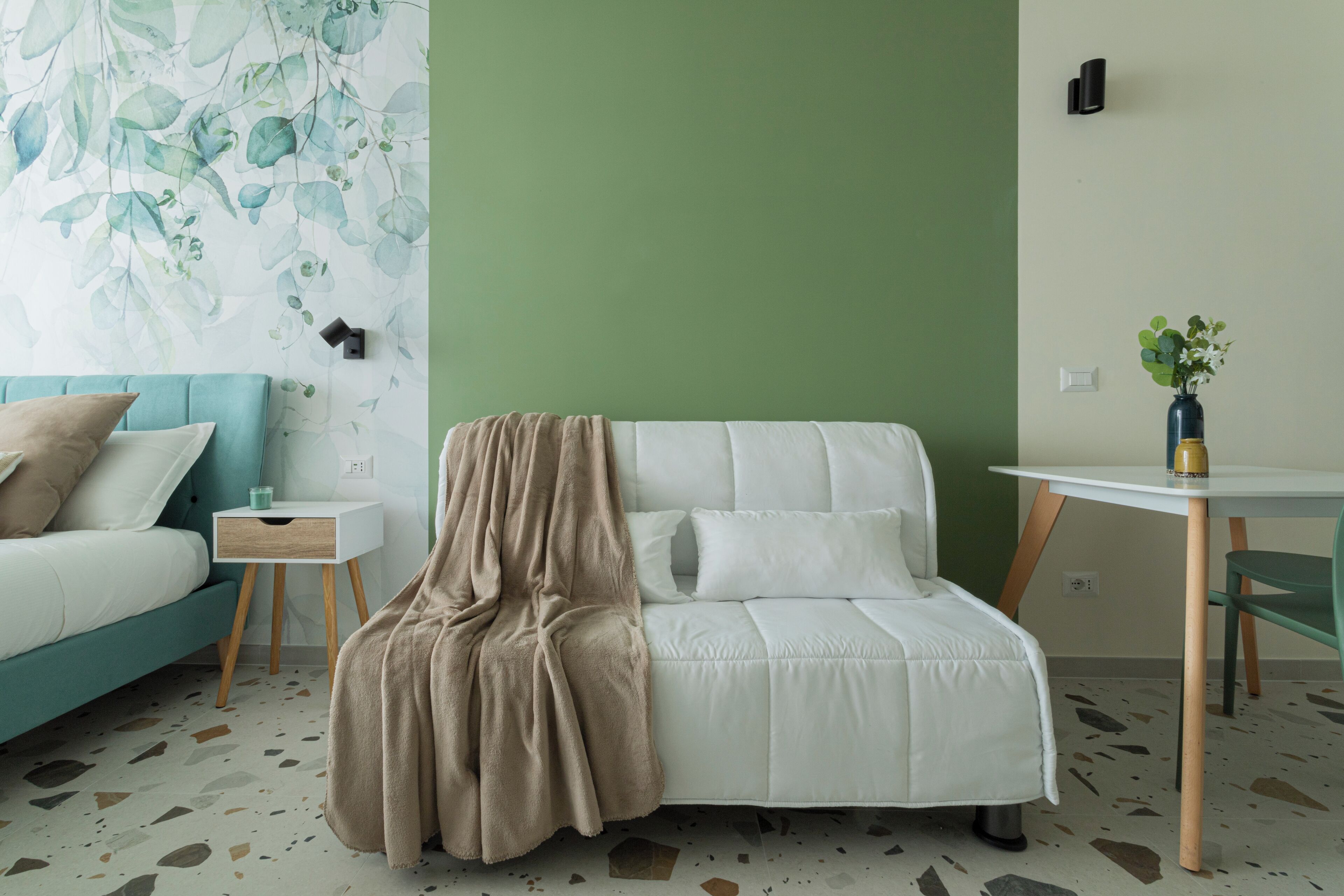 Une pièce moderne avec un canapé turquoise, un canapé blanc agrémenté d’un plaid beige, une petite table blanche et une chaise verte.