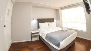 A bedroom with a bed, bedside tables, a nightstand, a window, and a door. - TERRAZAS DEL SOL (Arequipa)