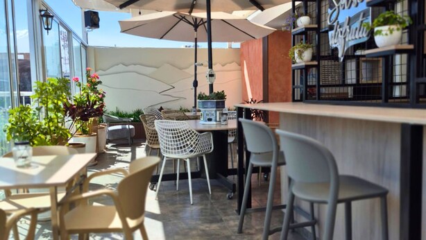 An outdoor café with tables and chairs, a bar area with shelves of plants, and a large umbrella providing shade. - TERRAZAS DEL SOL (Arequipa)