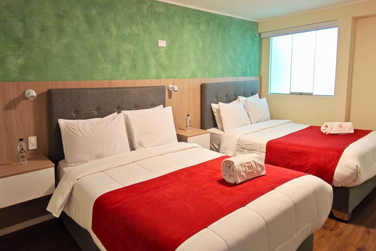 Ein Hotelzimmer mit zwei Betten, einer grünen Wand, einem Fenster und einem Holzboden.