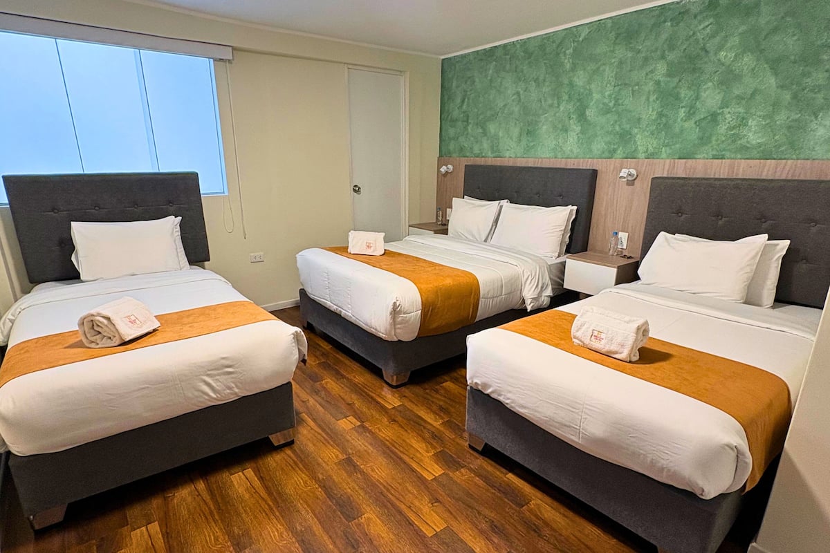 Ein Hotelzimmer mit drei Betten, Holzboden und einer Wand mit grüner Struktur.