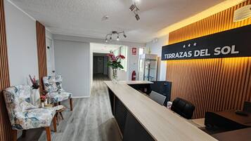 A reception area with a wooden reception desk, two patterned chairs, a vase with flowers, and a sign reading 'TERRAZAS DEL SOL'.