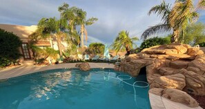 A pool area with lounge chairs, palm trees, and a rock formation.