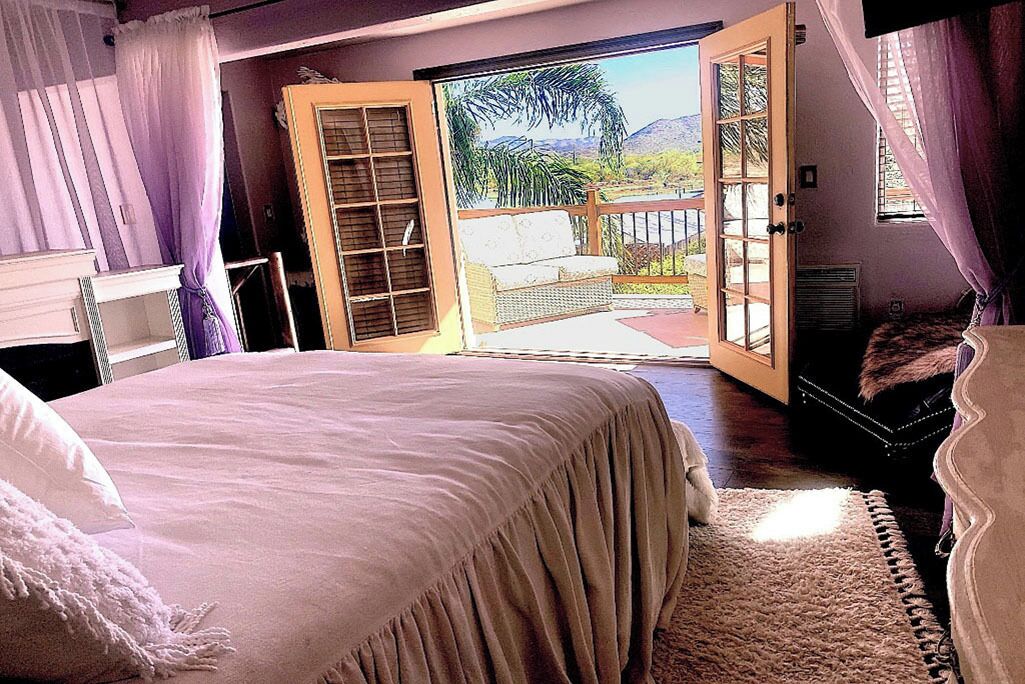 Un dormitorio con una cama grande, un ventanal corredero que da a un balcón y vistas al exterior.