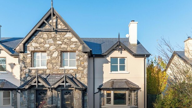 A stone house with a gabled roof, multiple windows, and a chimney.
