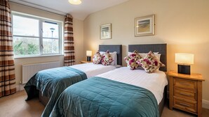 A hotel room with two beds, a window with curtains, a radiator, and framed pictures on the wall.