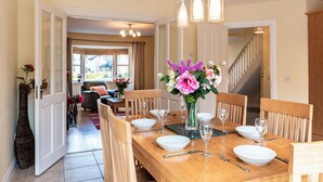 A dining area with a wooden table set for four, a vase of flowers, and a staircase in the background.