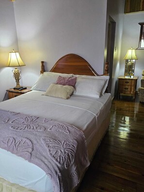 A neatly made bed with a wooden headboard, two bedside tables with lamps, and a wooden floor.