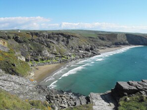 A coastal landscape with rocky cliffs, a beach, and a clear blue sea. - Atlanta (Tintagel)