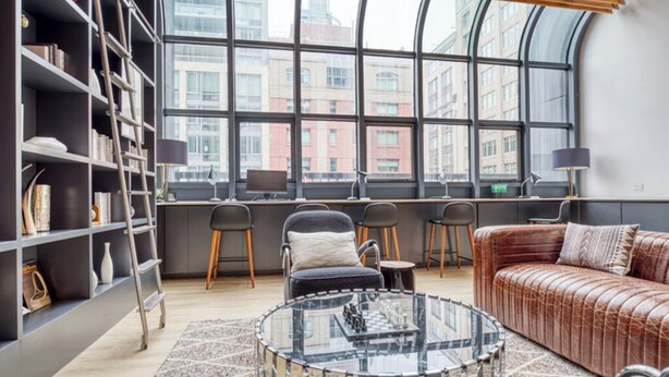 Un salon moderne doté d’un mur en verre incurvé, d’un canapé en cuir, d’une table basse en verre et d’une bibliothèque.
