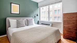 Une chambre à coucher avec un lit, une fenêtre avec des stores, un radiateur et une armoire en bois.