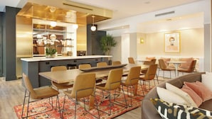 Un espace repas moderne avec une longue table et des chaises, une cuisine avec un bar et un coin salon confortable avec un canapé et des coussins.