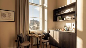 A dining area with a table and chairs, a window with curtains, and a kitchen area with cabinets and shelves.