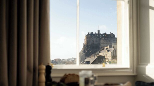 A view of a historic castle through a window, with a table and a chair in the foreground.