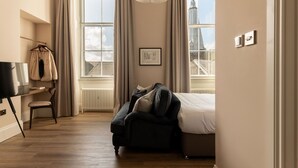 A bedroom with a bed, a chair, a desk, and a window with curtains.