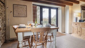 A dining area with a wooden table set for four, a stone wall, and a window with curtains.