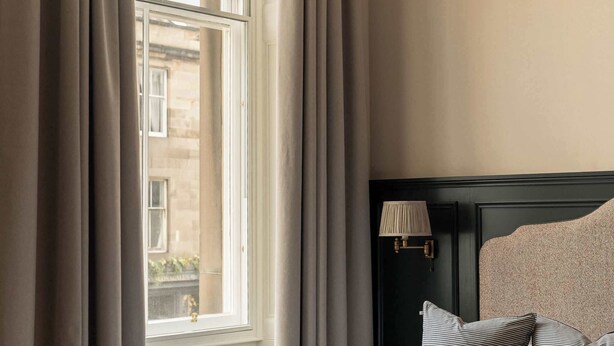 Une chambre d’hôtel avec un lit, une table de chevet avec une lampe, une fenêtre avec des rideaux et une vue sur l’extérieur.