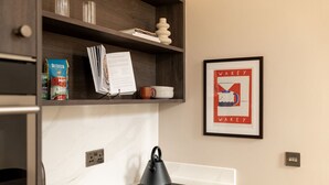 Une cuisine avec un plan de travail blanc, une bouilloire noire et une affiche encadrée accrochée au mur.