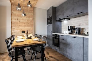 Een moderne keuken met donkere kastjes, een houten eettafel met stoelen en hanglampen.