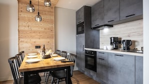 Una cocina moderna con armarios oscuros, una mesa de comedor de madera y lámparas colgantes.