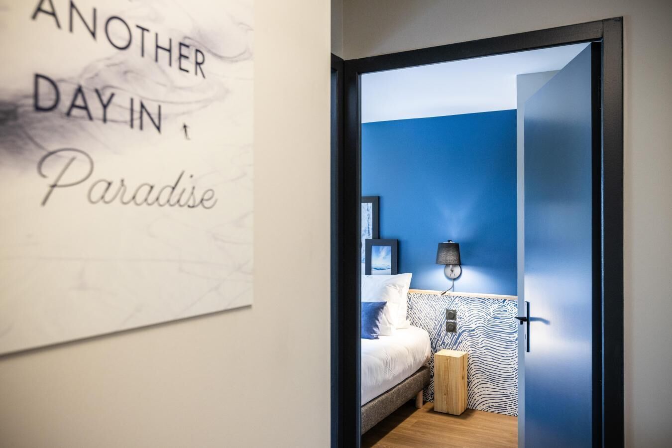 A bedroom with a bed, a nightstand, a lamp, and a wall with a text sign.