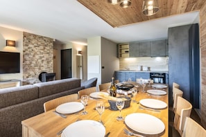 Een moderne eetruimte met een houten tafel voor zes personen, een accentmuur van steen en een keuken op de achtergrond.
