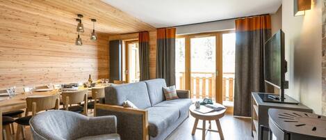 A modern living room with a sofa, armchairs, a dining table, and a TV.