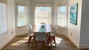 A dining room with a rectangular table, six chairs, and large windows with blinds. - The Pink House - beautiful beach stay! (Galveston)