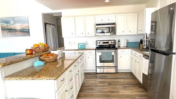 A modern kitchen with white cabinets, stainless steel appliances, and a granite countertop. - The Pink House - beautiful beach stay! (Galveston)
