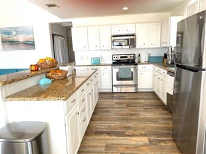 A modern kitchen with white cabinets, stainless steel appliances, and a granite countertop. - The Pink House - beautiful beach stay! (Galveston)
