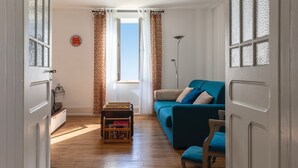 Ein Wohnzimmer mit einem blauen Sofa, Holzboden, einem kleinen Tisch mit einer Schachtel und einem Fenster mit Vorhängen.