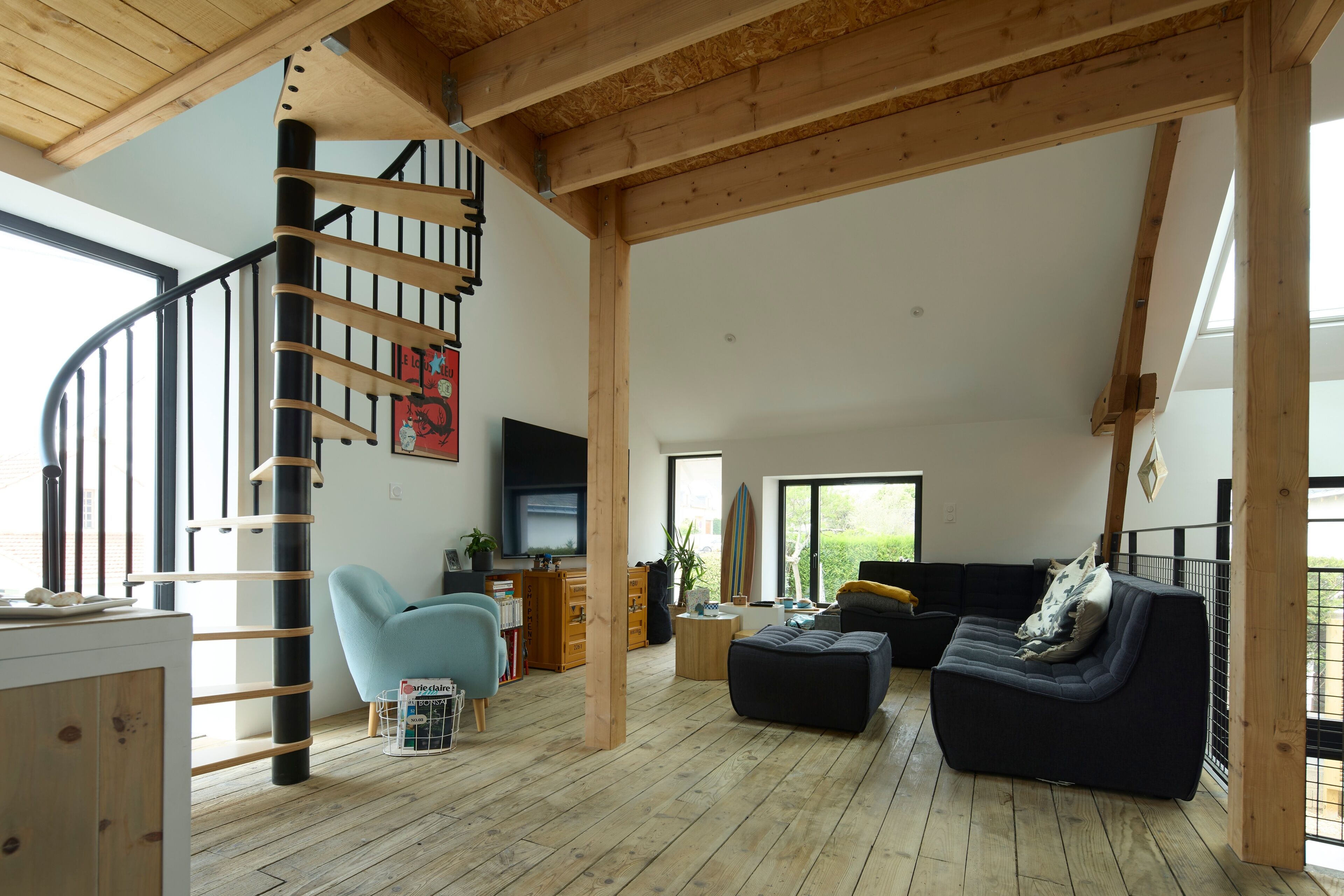 A spacious living area with a wooden staircase, a black sofa, a blue armchair, and a television.