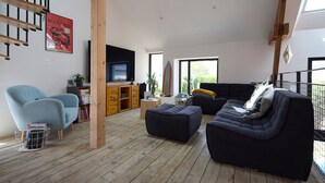 Een moderne woonkamer met een houten vloer, een blauwe fauteuil, een zwarte bank, een televisie en een boekenkast.
