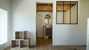 Een kamer met een houten plafond, een witte muur en een grote spiegel. Er zijn twee houten planken en een deur naar een andere kamer.