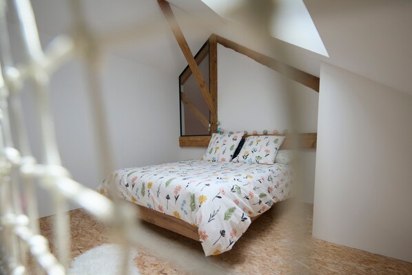 Une chambre avec un plafond en pente, des poutres en bois, un lit avec une literie à motifs floraux et une petite fenêtre.