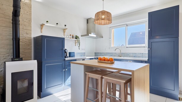 A modern kitchen with a central island, dark blue cabinets, a built-in stove, and a window providing natural light.