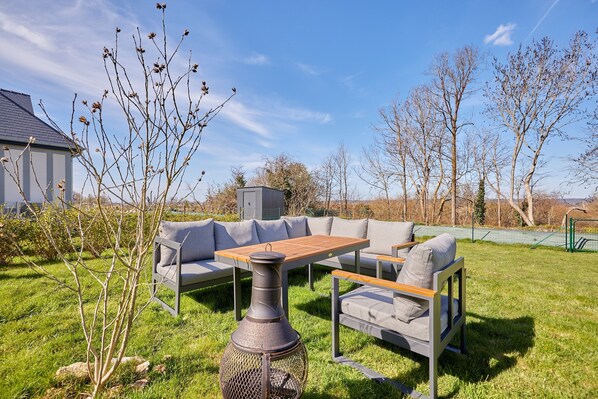 An outdoor seating area with a table and two sofas, surrounded by grass and trees. - Les Embruns du Clos - A 1 km des rives de la Seine (Berville-sur-Mer)