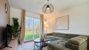 A living room with a sectional sofa, a TV, a small table, and a potted plant.