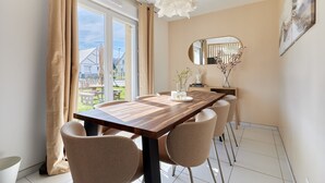 A dining area with a wooden table and beige chairs, a hanging light fixture, a mirror, and a view of the outdoors.