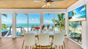 A dining area with a view of the ocean, a ceiling fan, and a large window with a view of the beach.