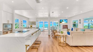 A modern kitchen with a central island, a dining area with a view, and a living room with a sofa and coffee table.