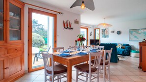 A dining area with a wooden table set for four, surrounded by white chairs. - Ty Kéréré - Maison 3★ - Calme, Grand Jardin Arboré, 500m plage (Locmariaquer)