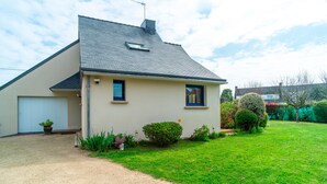 A single-story house with a sloped roof, a garage, and a well-maintained lawn. - Ty Kéréré - Maison 3★ - Calme, Grand Jardin Arboré, 500m plage (Locmariaquer)
