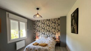 Een slaapkamer met een bed, een raam, behang met een patroon, een hanglamp en een schilderij aan de muur.
