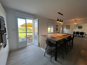 Une cuisine moderne dotée d’un grand îlot central, de portes-fenêtres coulissantes donnant sur un patio, et d’un coin repas avec une table et des chaises.