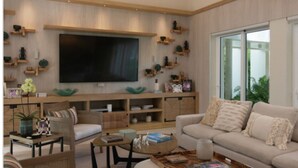 A modern living room with a large flat-screen TV, wooden shelving with decorative items, a beige sofa, and a coffee table.