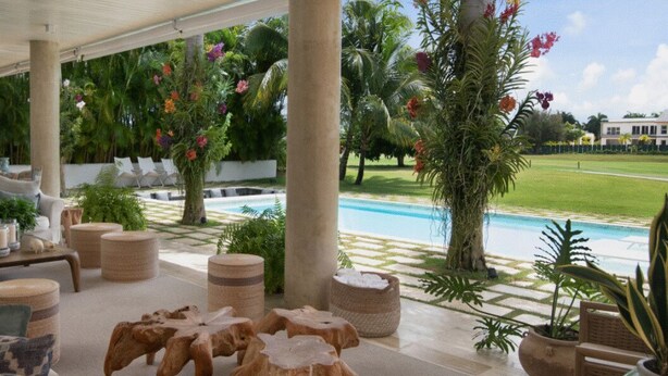 A covered outdoor area with lounge chairs, a pool, and tropical plants.